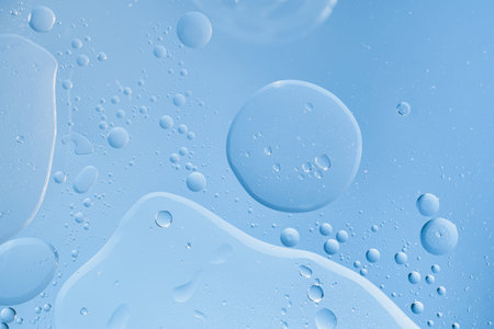Water and oil droplets mixing on blue surface forming an abstract liquid background