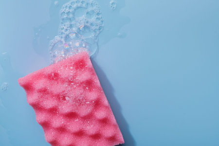 Colorful cleaning sponge with soap bubbles on blue background