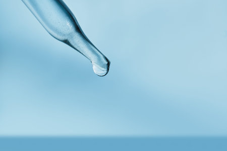 Pipette dripping single drop of liquid on light blue background
