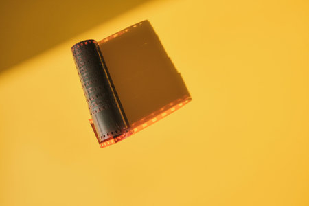 Film strip with perforations unrolling against yellow background, showing analog photography concept