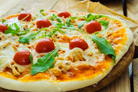 Round pizza with cheese and tomatoes on a wooden table, green basil leaves.の写真素材