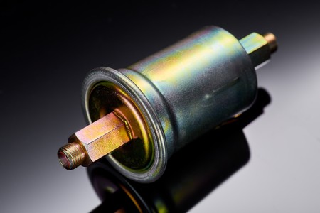 A new fuel filter enclosed in a metal casing with an inlet and outlet on fuel lines on a dark backgroundの写真素材