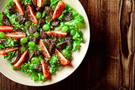 warm salad with chicken liver and grapes on a wooden table close-upの写真素材