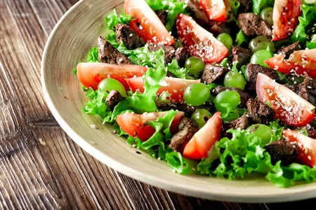 warm salad with chicken liver and grapes on a wooden table close-upの写真素材