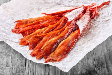 Fresh hot and cold smoked fish lies on a paper napkin on a wooden tableの写真素材