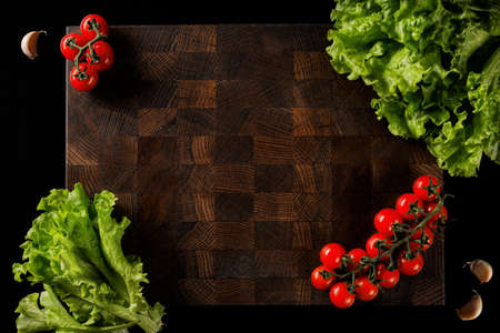 Handmade wooden chopping board with fresh vegetables on a dark background. space for labels