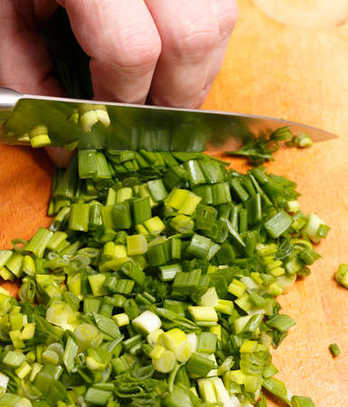 Cut green onion with a kitchen knife on a wooden cutting board. Fresh green onions on a cutting board. Cutted Green Onions On Wooden Cutting Boardの写真素材