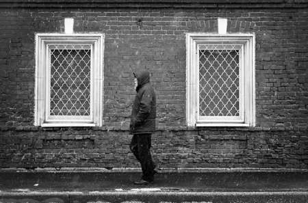 Townspeople. A lonely man in snowy weather against a brick wall background with two windows. Snowy weather. A man goes about his business. The townspeople are in a bad weather. The man is hurrying about his business.の写真素材