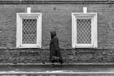 Townspeople. A lonely woman in snowy weather against a brick wall background with two windows. Snowy weather. Woman goes about her business. The townspeople are in a bad weather. Woman is hurrying about her business.の写真素材