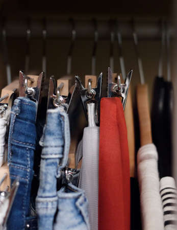Various clothes hanged in wardrobe. Clothes hang in the closet. Jeans and skirts on chrome plated clothespins. Tightly hanging clothes in the wardrobe.の写真素材