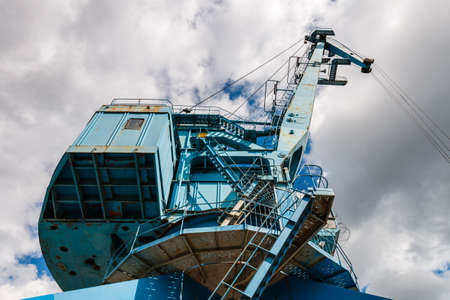 Blue crane on the river. Picturesque blue port crane on a background of blue sky with clouds....