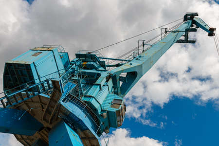 Blue crane on the river. Picturesque blue port crane on a background of blue sky with clouds. Designs of a metal port crane. Industrial Design. Industrial shipyard crane in Moscow, Russia.の写真素材