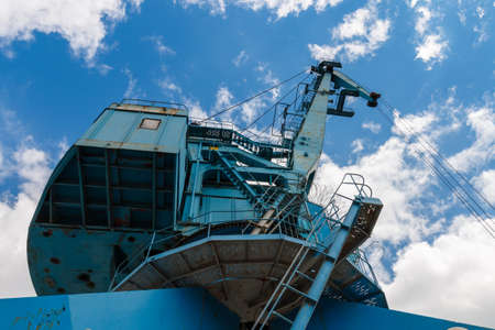 Blue crane on the river. Picturesque blue port crane on a background of blue sky with clouds. Designs of a metal port crane. Industrial Design. Industrial shipyard crane in Moscow, Russia.の写真素材
