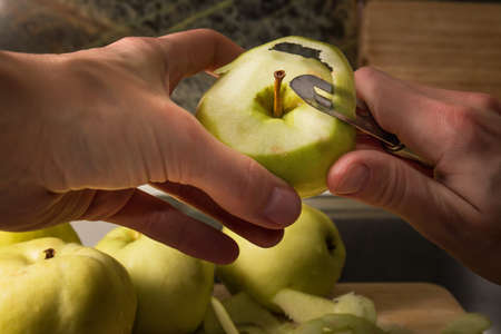Female hands peeling skin off of green apple using a paring knife. Peel the Skin Off Apples. Woman cuts off the peel of an apple. Garden apples. Golden apples. Farm products. Juicy fruit.の写真素材