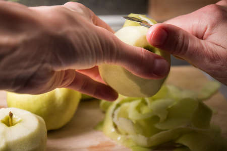 Female hands peeling skin off of green apple using a paring knife. Peel the Skin Off Apples. Woman cuts off the peel of an apple. Garden apples. Golden apples. Farm products. Juicy fruit.の写真素材