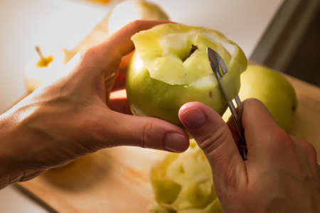 Female hands peeling skin off of green apple using a paring knife. Peel the Skin Off Apples. Woman cuts off the peel of an apple. Garden apples. Golden apples. Farm products. Juicy fruit.の写真素材