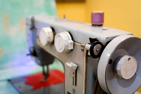 Old sewing machine with a coil of crimson threads on a yellow and turquoise background.の写真素材