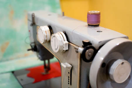 Old sewing machine with a coil of crimson threads on a yellow and turquoise background.の写真素材