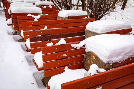 Red wooden benches covered with snow. Series of benches in a winter park.の写真素材