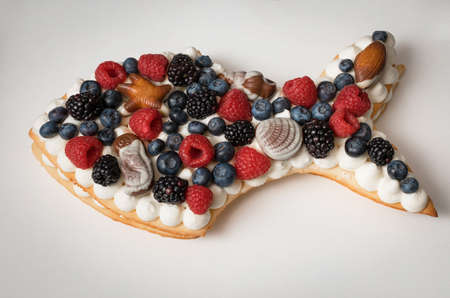 Handmade cake in the form of fish. Puff cake with cream decorated with sea theme. Cake decorated with raspberries, blueberries, blackberries, and chocolates. Cake for Pisces.の写真素材