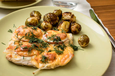 Baked pork with cheese, tomatoes, onions and Brussels sprouts. Serving with green plates. A glass of mineral water. Freshly baked bread.の写真素材