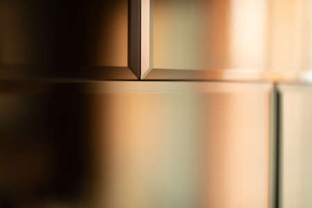 The surface of the mirror tiles. Wall of mirrored tiles with edges. Interior design with sunset lighting. Rows of mirror tiles. Abstraction of tiles with sharp edges. Gold backgroundの写真素材