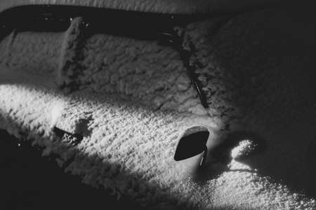 Snow covered old classic car illuminated by a ray of light at night. Old car covered with snow. Soviet car Volga. Details of a car covered with snowの写真素材