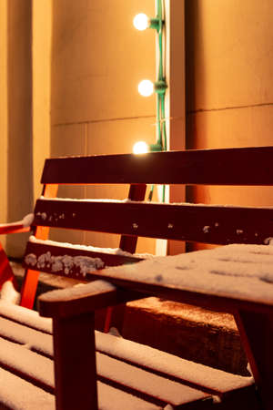 Wooden red bench and a table at outdoor cafe covered with snow in the winter in the off-season. City street in the evening in winter. Russia, Moscow.の写真素材