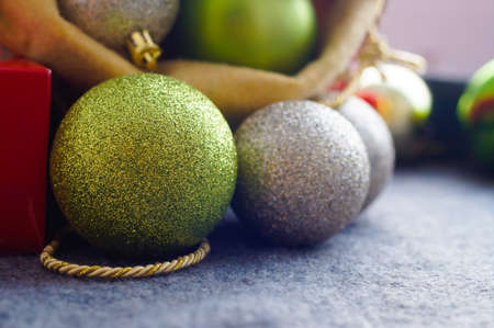 Christmas golden, silver and green decoration balls and red gift box on grey, front view