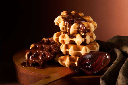 Belgian waffles in chocolate syrup piled on wooden boardの写真素材
