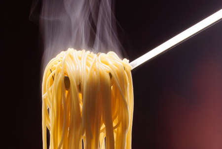 Steaming pasta in a spaghetti spoon on brown backgroundの写真素材