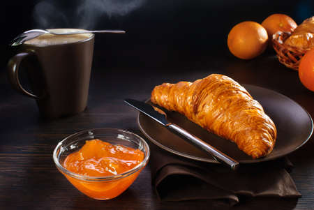 breakfast croissant, apricot jam and cup of coffee and milkの写真素材