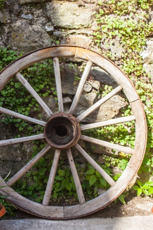 Old wooden wheel leaning up against stone wallの写真素材