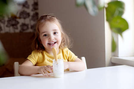 Cheerful little girl eating plain homemade yogurt using spoon. Healthy smiling kid, organic natural foodの写真素材