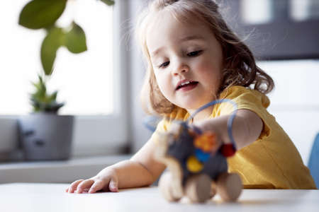 Close-up portrait of cute little girl playing with toy. Kid in yellow t-short excited game