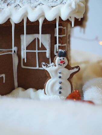 Gingerbread snowman with white icing in front of a gingerbread house with lightsの写真素材