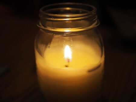 Burning candle in jar at night, in the dark. Golden light of candle flameの写真素材