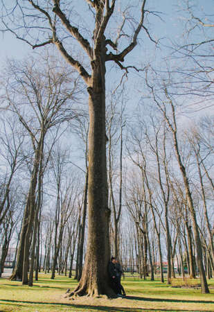 A beautiful loving couple smiling and kissing a large tree in the park.