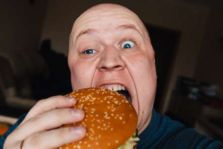 The eating of a hamburger by a man with a terrible expression.の写真素材