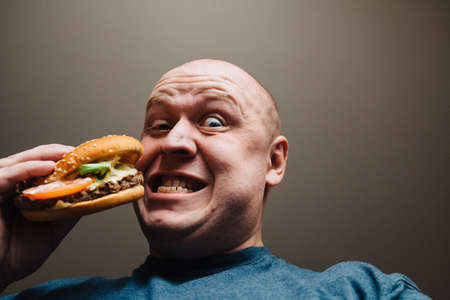The eating of a hamburger by a man with a terrible expression.の写真素材