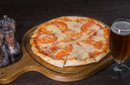 Hot piece of pizza with melted cheese on a rustic wooden table and beer.の写真素材