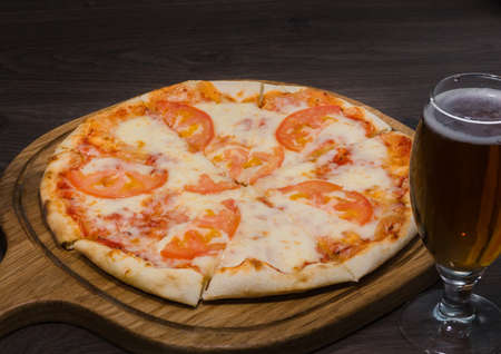 Hot piece of pizza with melted cheese on a rustic wooden table and beer.の写真素材