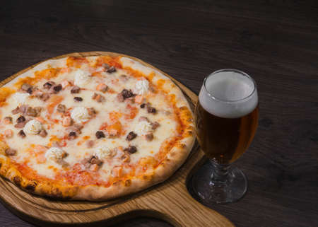 Hot piece of pizza with melted cheese on a rustic wooden table and beer.の写真素材