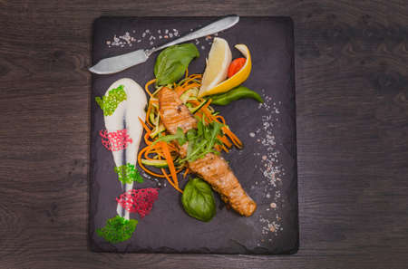 Salmon steak with lemon greens and sauce on stone with salt.の写真素材