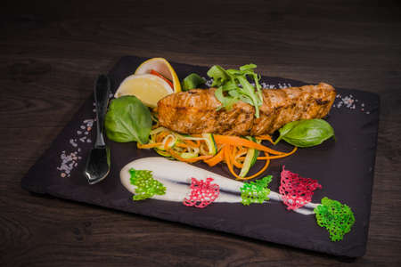 Salmon steak with lemon greens and sauce on stone with salt.の写真素材