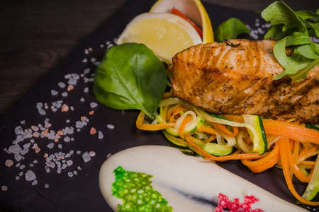 Salmon steak with lemon greens and sauce on stone with salt.の写真素材