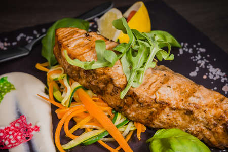 Salmon steak with lemon greens and sauce on stone with salt.の写真素材
