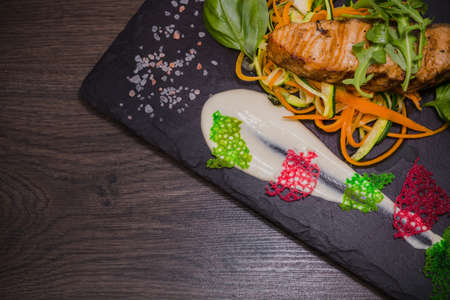 Salmon steak with lemon greens and sauce on stone with salt.の写真素材