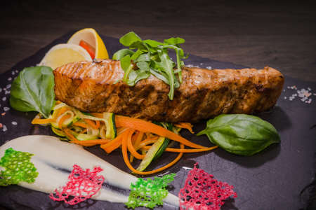 Salmon steak with lemon greens and sauce on stone with salt.の写真素材