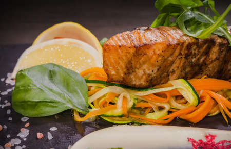 Salmon steak with lemon greens and sauce on stone with salt.の写真素材